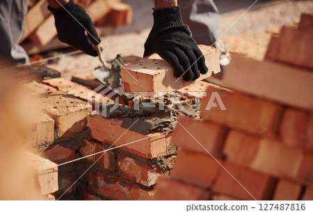 In gloves, holding brick. Close up view of man that is working on the construction site 127487816