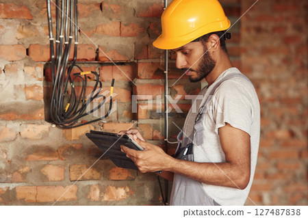Digital tablet in hands. Handsome Indian man is on the construction site 127487838