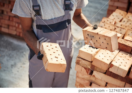 With brick in hands. Close up view of man that is working on the construction site 127487847