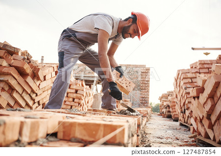 Side view, working and placing the bricks. Handsome Indian man is on the construction site Side view, working and placing the bricks. Handsome Indian man is on the construction site 127487854