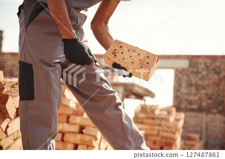 With brick in hands. Close up view of man that is working on the construction site 127487861