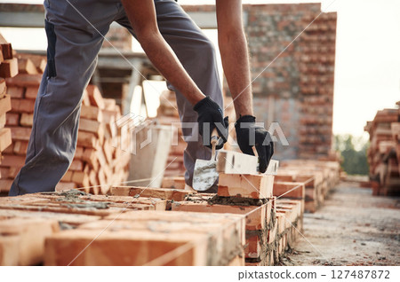 In gloves, holding brick. Close up view of man that is working on the construction site 127487872