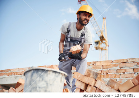 Blue sky and crane is behind. Handsome Indian man is on the construction site 127487883