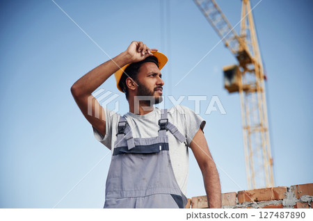 Taaking a break. Standing against crane and blue sky. Handsome Indian man is on the construction site 127487890