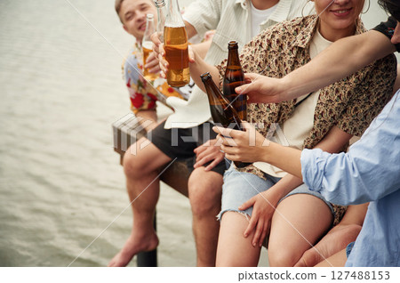 Group of friends are sitting near the lake with beer in hands 127488153