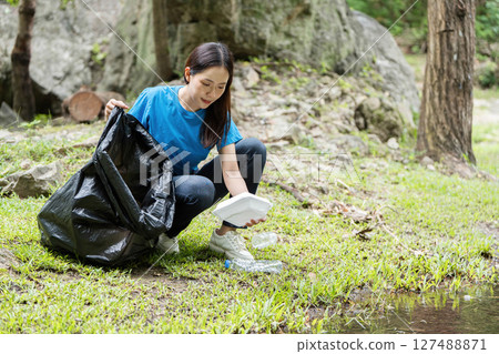 Environmental Volunteerism. A woman engaged in waste collection at a natural site. Environmental Volunteerism. A woman engaged in waste collection at a natural site. 127488871