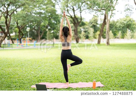 Yoga and mindfulness. Young woman in tree pose outdoors in a park. 127488875