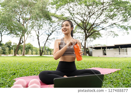 Joyful yoga practice. A woman smiles while sitting on a yoga mat and opening her water bottle. 127488877