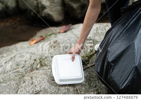 Individual Picking Up Food Container During Clean-Up. Volunteer collecting waste from rocky area. 127488879