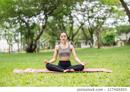 Yoga practice in nature. Young woman meditating peacefully on a yoga mat outdoors. 127488893