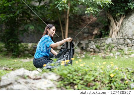 Volunteer cleaning nature. Young woman collecting trash in a park. 127488897