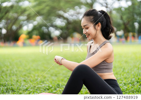 Yoga and Mindfulness. Young woman smiling while practicing yoga stretches outdoors with a laptop. 127488919