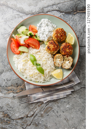 Greek chicken meatballs with feta cheese served with lemon rice and vegetable salad close-up in a plate. vertical top view 127489390