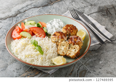 Spicy Greek Chicken meatballs stuffed with feta cheese served with lemon rice, tzatziki sauce and fresh salad close-up in a plate. horizontal 127489395