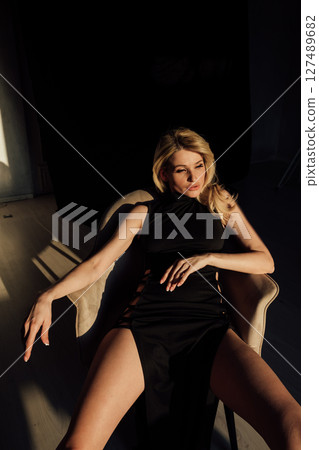 Slim woman in black evening dress sitting on chair 127489682