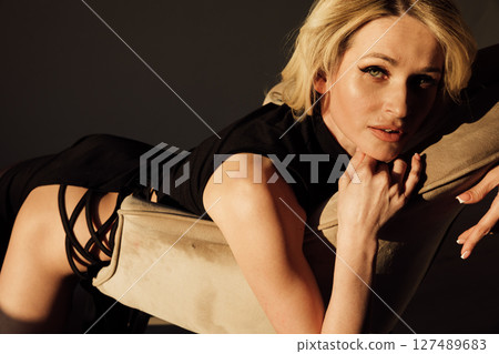 Slim woman in black evening dress sitting on chair 127489683