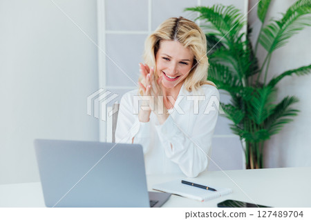 woman working on laptop and smiling at desk in office online woman working on laptop and smiling at desk in office online 127489704