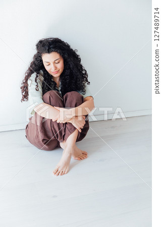 Portrait of a beautiful curly brunette woman in summer clothes sitting on the floor 127489714