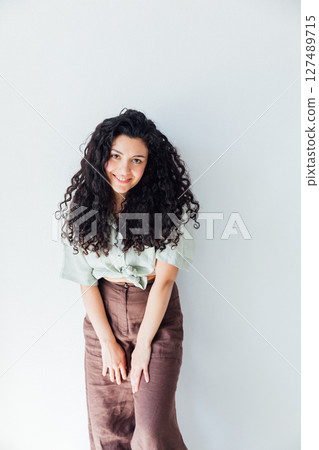 Curly brunette woman in clothes smiling on white background 127489715