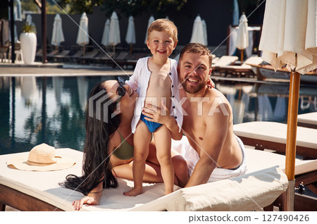 Cheerful people are sitting. Happy family of father, mother and son are in the pool 127490426