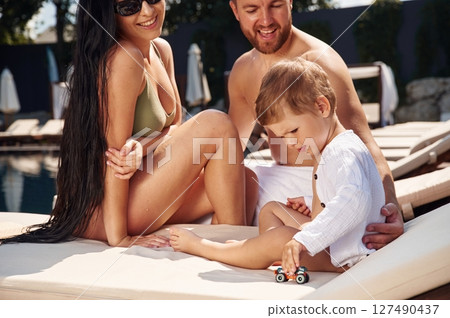 Cheerful people are sitting. Happy family of father, mother and son are in the pool 127490437