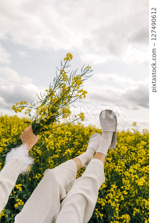 Person holding flowers while lying in a field of yellow blooms on a cloudy day 127490612