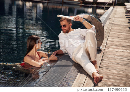 With newspaper in hand. Man with woman is in the pool together 127490633