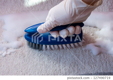 Hand in rubber glove with brush for cleaning. Plastic blue brush for cleaning on the floor. House cleaning concept. 127490719