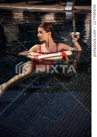 With drink in hand. Young woman in red swimsuit is in the pool With drink in hand. Young woman in red swimsuit is in the pool 127490856
