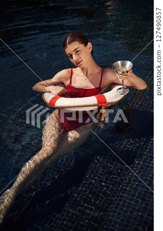 With drink in hand. Young woman in red swimsuit is in the pool 127490857