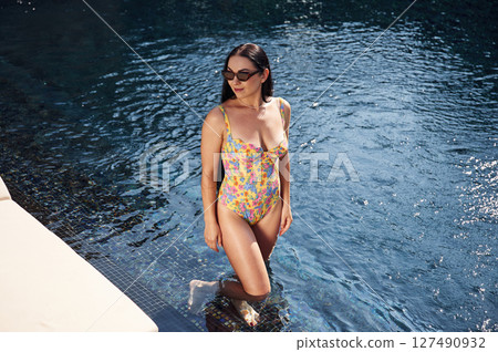 Beautiful woman that is in swimsuit is in the pool Beautiful woman that is in swimsuit is in the pool 127490932