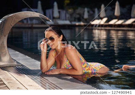 Standing, leaning on the surface. Beautiful woman that is in swimsuit is in the pool Standing, leaning on the surface. Beautiful woman that is in swimsuit is in the pool 127490941