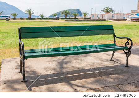 Green wooden bench in sunny coastal park. Public space, relaxation area, and outdoor urban furniture near the sea. Green wooden bench in sunny coastal park. Public space, relaxation area, and outdoor urban furniture near the sea. 127491009