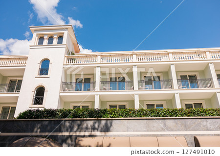 Elegant coastal building with balconies and decorative tower. Mediterranean architecture, hotel facade, and sunny travel destination. Elegant coastal building with balconies and decorative tower. Mediterranean architecture, hotel facade, and sunny travel destination. 127491010