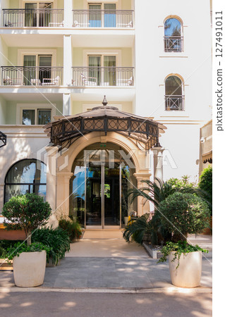 Hotel entrance with decorative canopy and manicured plants. Luxury hospitality, architectural detail, and travel accommodation design Hotel entrance with decorative canopy and manicured plants. Luxury hospitality, architectural detail, and travel accommodation design 127491011
