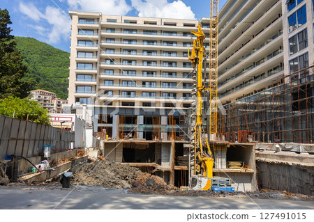 High-rise construction site in urban area. Modern development, civil engineering, and foundation work with industrial machinery. 127491015