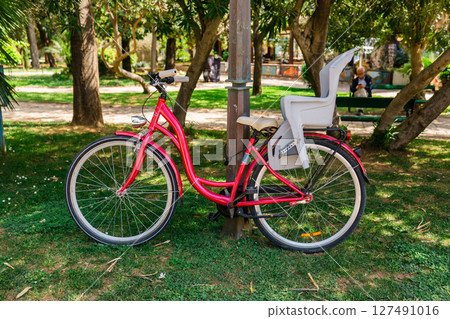 Parked red bicycle with child seat. Family lifestyle, eco-friendly transport, and urban leisure in green outdoor spaces. 127491016