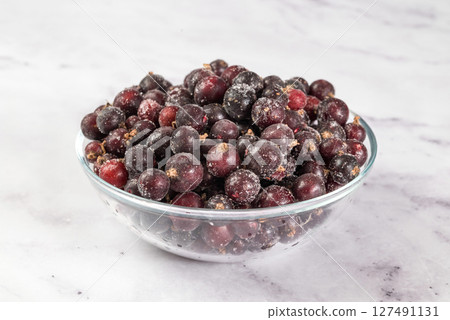 Frozen black currant berries on table in transparent bowl, on light background. Preservation of vegetables and fruits. Natural products Frozen black currant berries on table in transparent bowl, on light background. Preservation of vegetables and fruits. Natural products 127491131