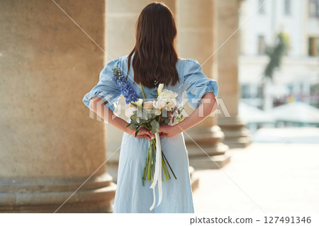 Holding flowers behind the back. Beautiful woman is outdoors Holding flowers behind the back. Beautiful woman is outdoors 127491346