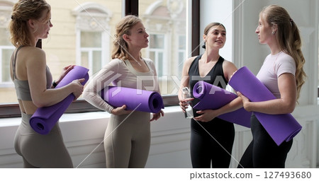 Women are chatting in bright yoga studio, holding mats. Concept of healthy lifestyles. Women are chatting in bright yoga studio, holding mats. Concept of healthy lifestyles. 127493680
