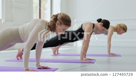 Group of young women are practicing yoga on mats in a large, bright room. Concept of healthy lifestyles and self development. Group of young women are practicing yoga on mats in a large, bright room. Concept of healthy lifestyles and self development. 127493729