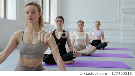 Women repeating asanas after female yoga coach, sitting on mats in bright studio with big windows. Concept of healthy lifestyles and self development. 127493818