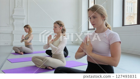 Women practicing yoga sitting in lotus pose meditation relaxing. Sporty women doing exercise in studio for class for yoga wellness mindfulness meditation. Women practicing yoga sitting in lotus pose meditation relaxing. Sporty women doing exercise in studio for class for yoga wellness mindfulness meditation. 127493831