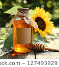 "Close-up of a glass jar filled with golden honey, wooden honey dipper dripping sweet liquid, surrounded by fresh flowers and tea cup, natural and healthy food concept, bright yellow tones, warm light 127493929