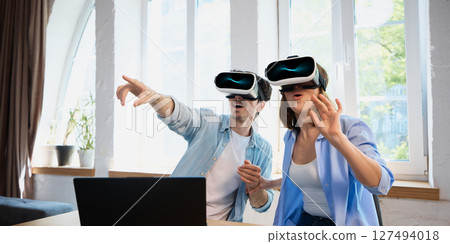 Couple immersed in virtual reality experience with headsets exploring digital world together 127494018