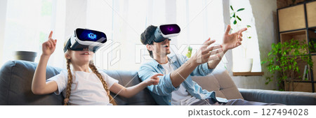 Father and daughter enjoying virtual reality headset experience in cozy living room setting Father and daughter enjoying virtual reality headset experience in cozy living room setting 127494028