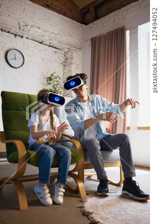 Father and daughter exploring virtual reality with headsets in cozy living room environment 127494052