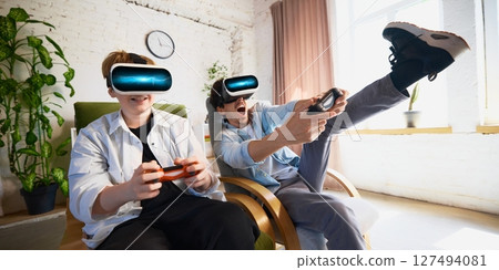 Father and son immersed in virtual reality gaming experience in cozy living room setting 127494081