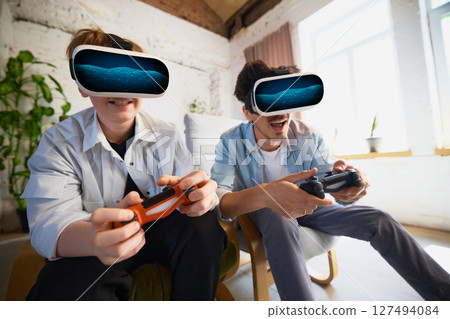 Father and son enjoying virtual reality gaming at home with controllers in bright living room 127494084