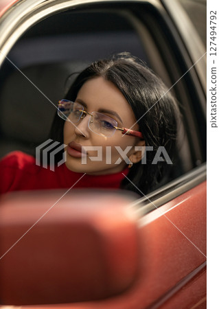 beautiful girl with glasses sits in the passenger seat of a car, gazing thoughtfully out the window as sunlight brightens her face and enhances her features beautiful girl with glasses sits in the passenger seat of a car, gazing thoughtfully out the window as sunlight brightens her face and enhances her features 127494792